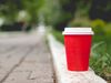 A red disposable coffee cup discarded by a road